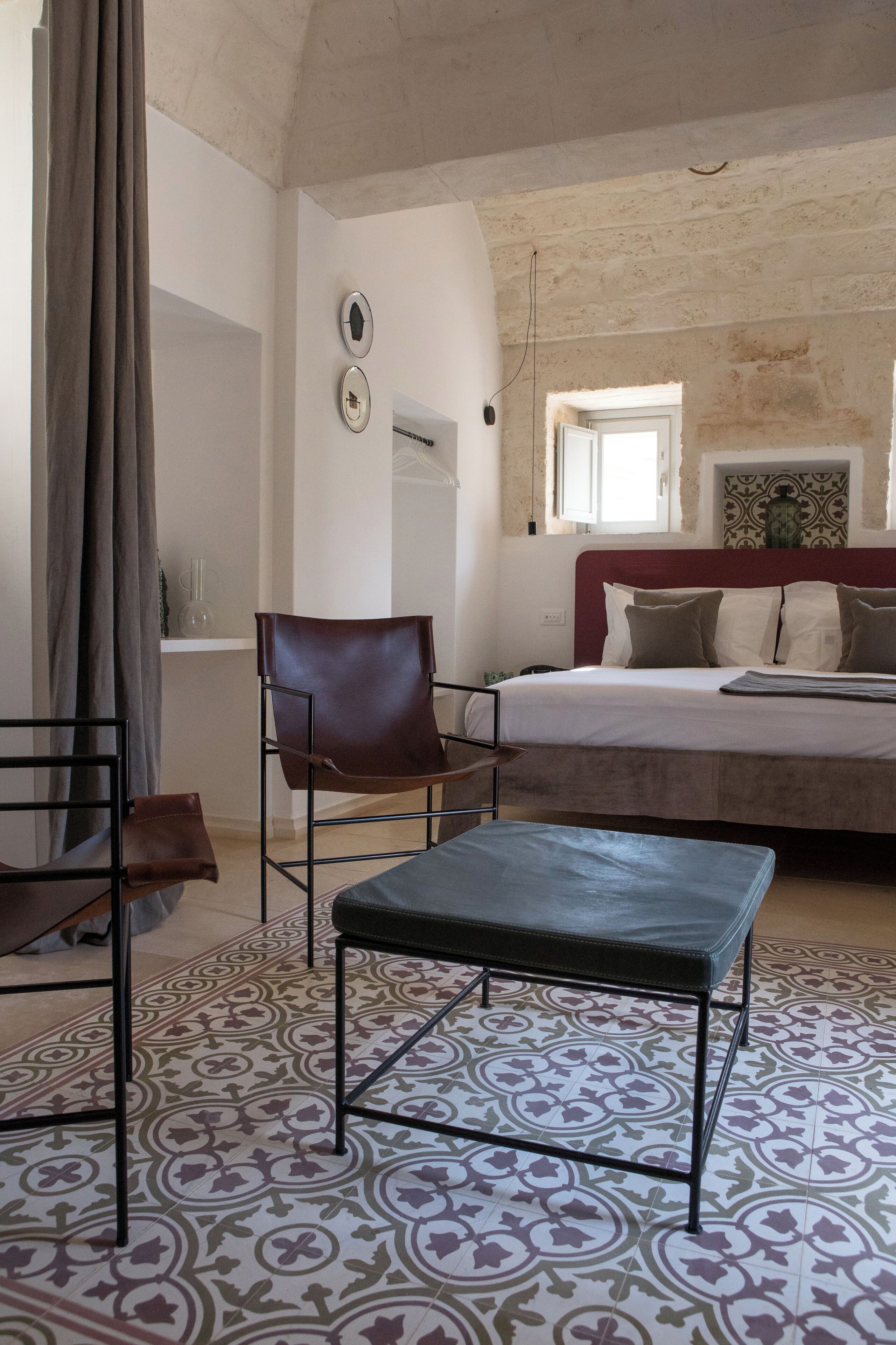 Une chambre à coucher comprenant un lit, une chaise, une table, des carreaux de sol à motifs et une fenêtre donnant sur un paysage agréable.