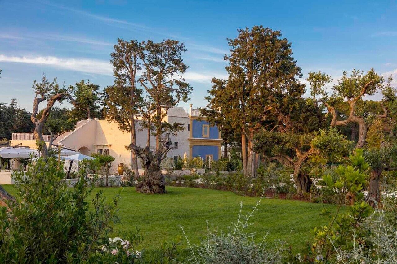 Um jardim com árvores e um edifício com fachada azul.