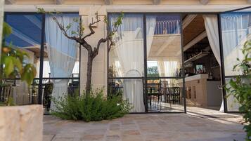 A modern building with large glass doors, a stone patio, and a small tree.
