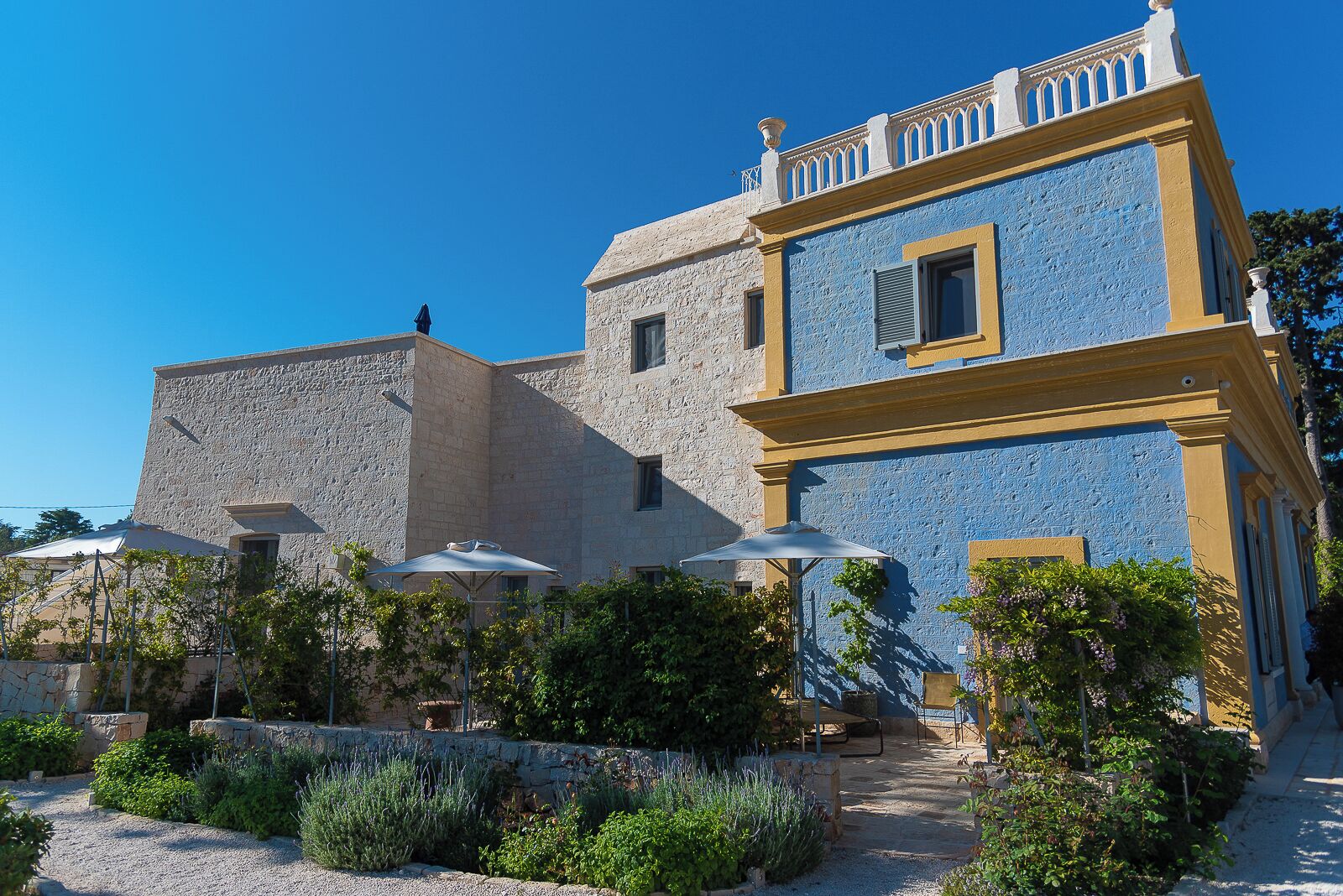 A building with a stone facade and a blue upper section, featuring outdoor seating with umbrellas.