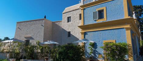 A building with a stone facade and a blue upper section, featuring outdoor seating with umbrellas.