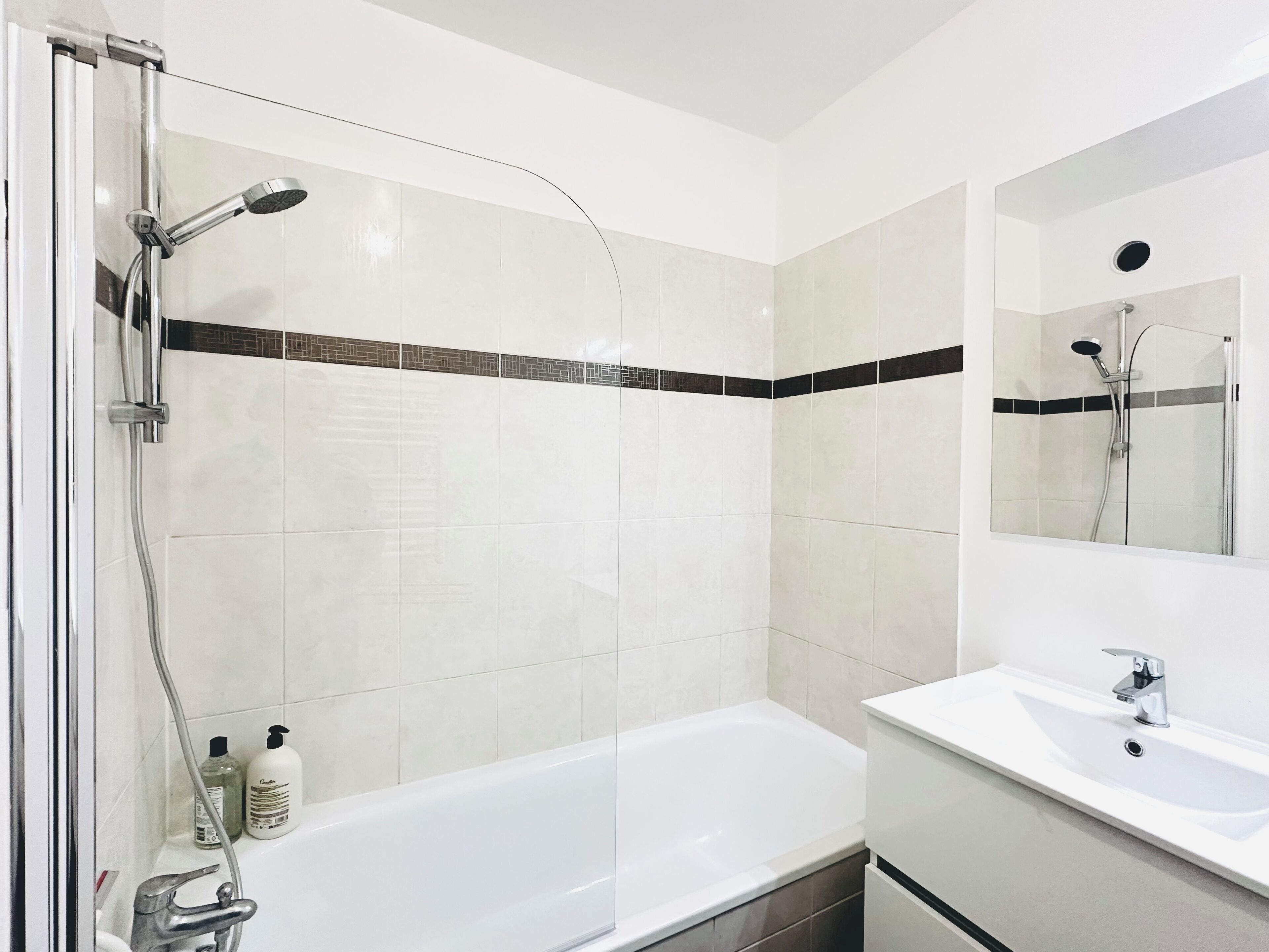 A modern bathroom with a glass-enclosed shower, a white bathtub, and a sink with a mirror above it.
