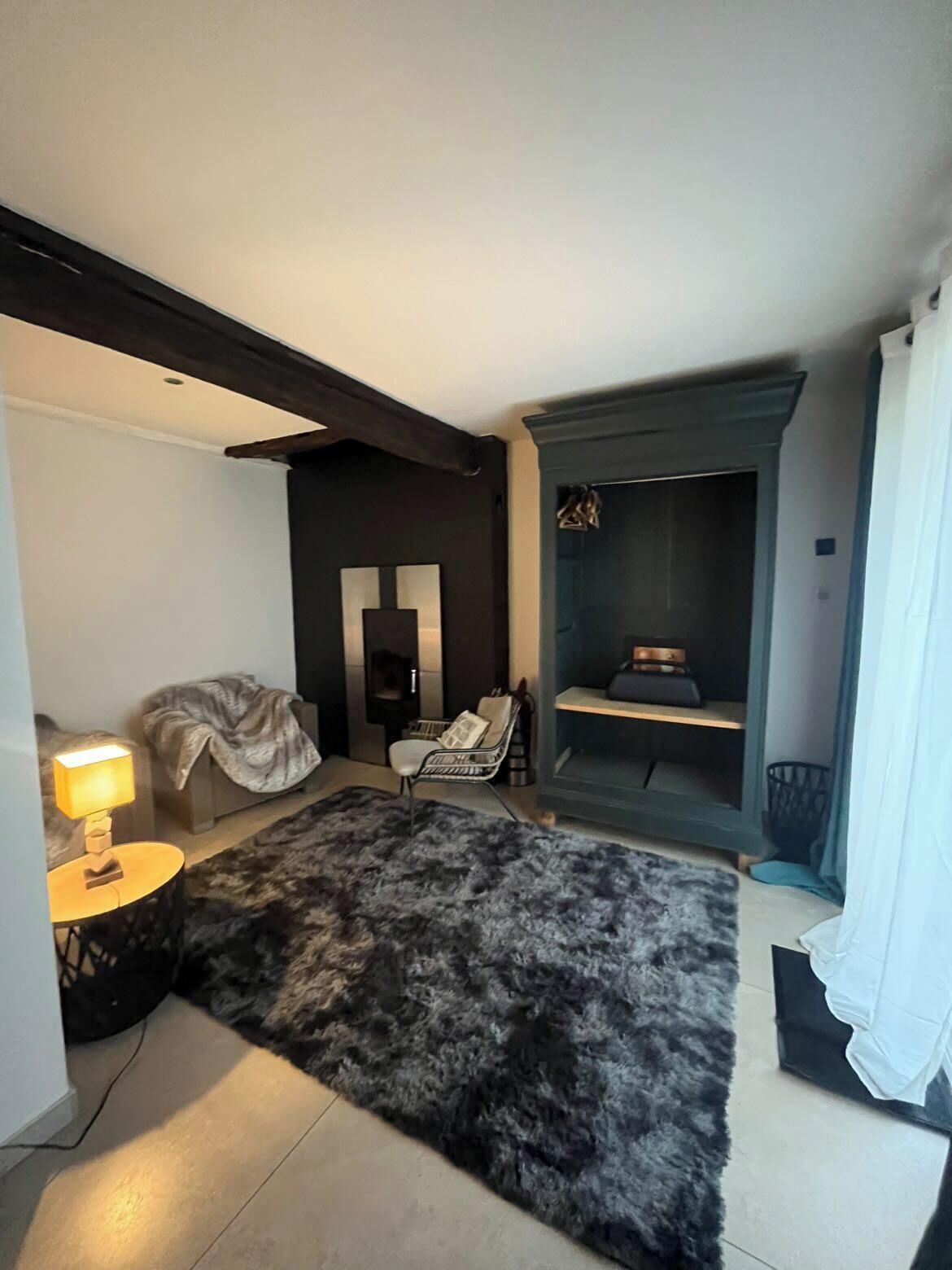 Uma sala de estar moderna com uma parede de destaque escura, uma lareira, um tapete macio e uma mesa lateral com abajur.