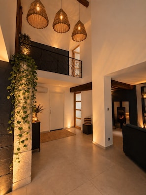 Un interior espacioso con un techo alto, una escalera que lleva a un balcón y una chimenea moderna.