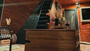 A wooden interior with a staircase, a wooden desk with a vase and wine glass, and a chair.