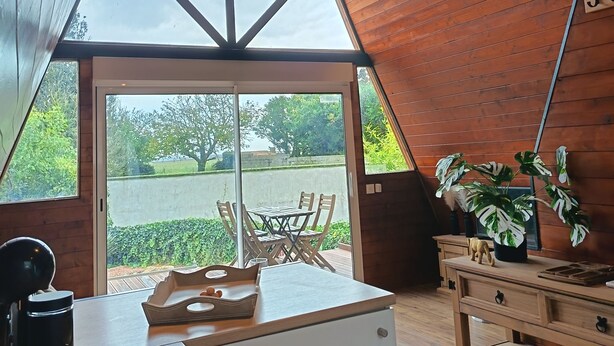 A room with a sloped ceiling, wooden walls, a large window, and a table with chairs.