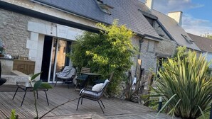 A pool area with a wooden deck, lounge chairs, and a stone building with a tiled roof.