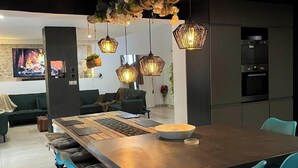 A modern kitchen with a central island, blue bar stools, hanging pendant lights, and a stone wall with a fireplace.