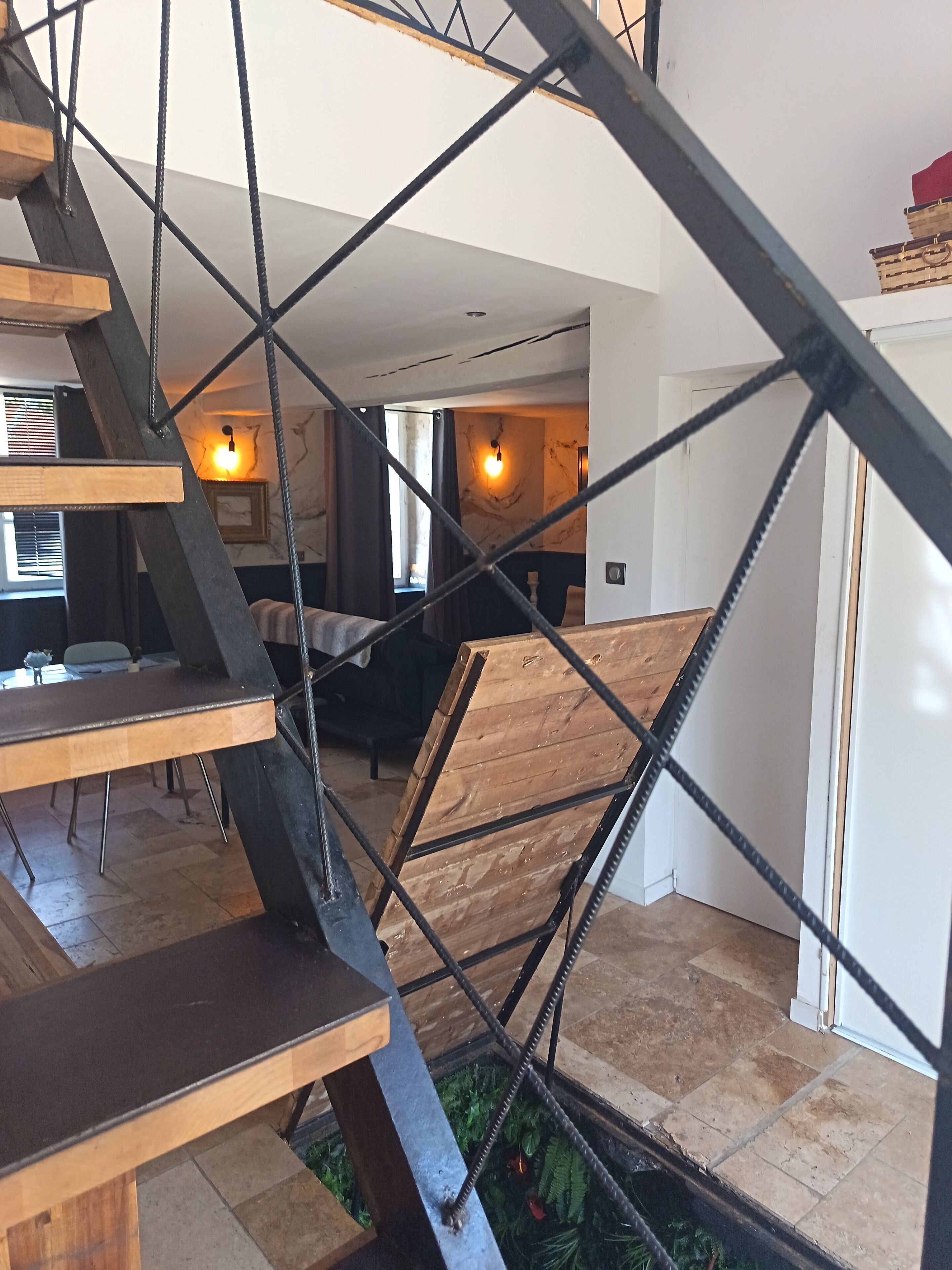 Un intérieur moderne avec un escalier dont les éléments en métal et en bois sont apparents, menant à un espace de vie comprenant un canapé et une table à manger.
