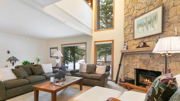 A cozy living room with a stone fireplace, two sofas, a coffee table, and a fireplace mantel with a clock and framed picture. - I1 Gore Creek Meadows 4 Bedroom Townhouse (Vail)