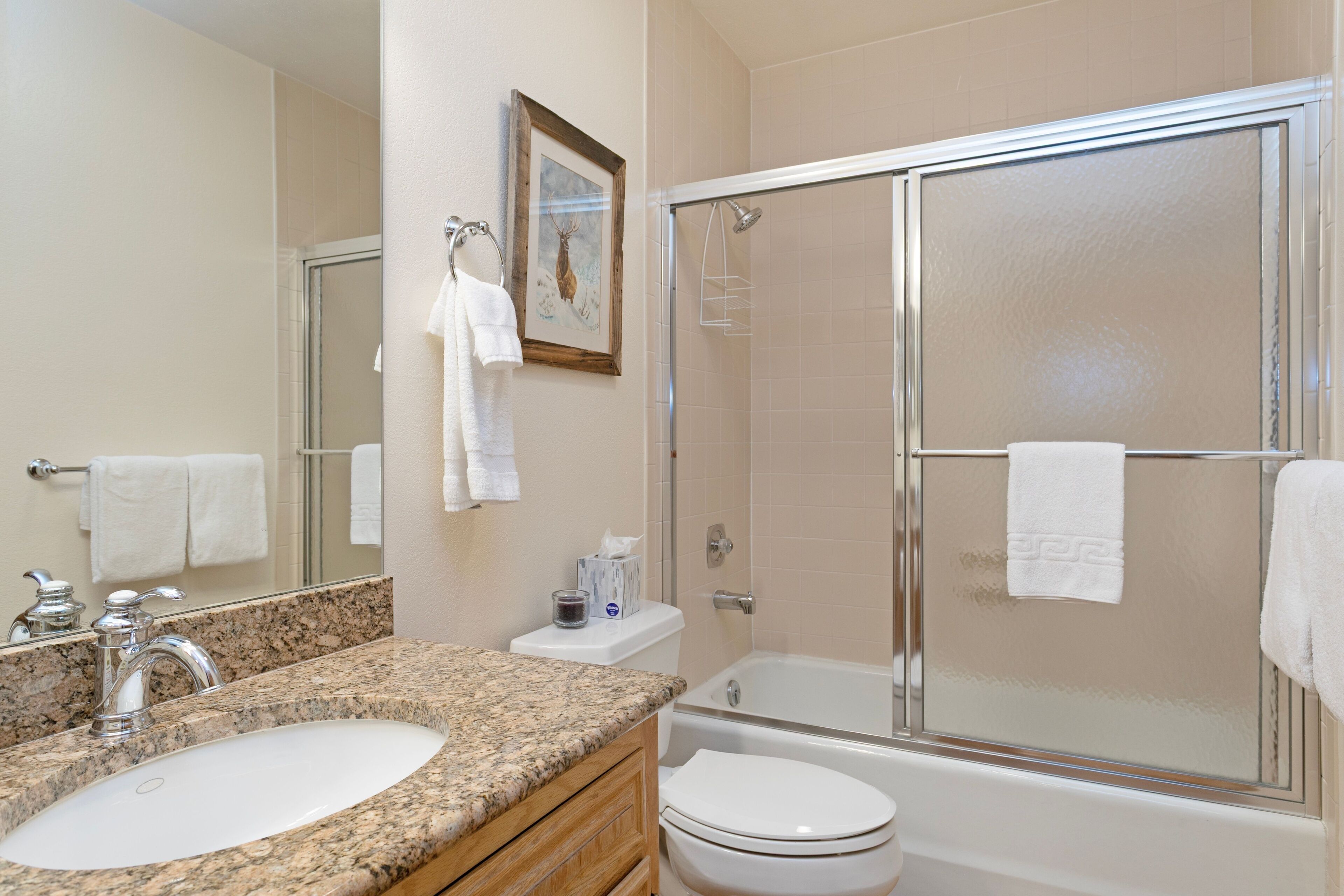 A bathroom with a granite countertop sink, a toilet, a bathtub, and a glass-enclosed shower.