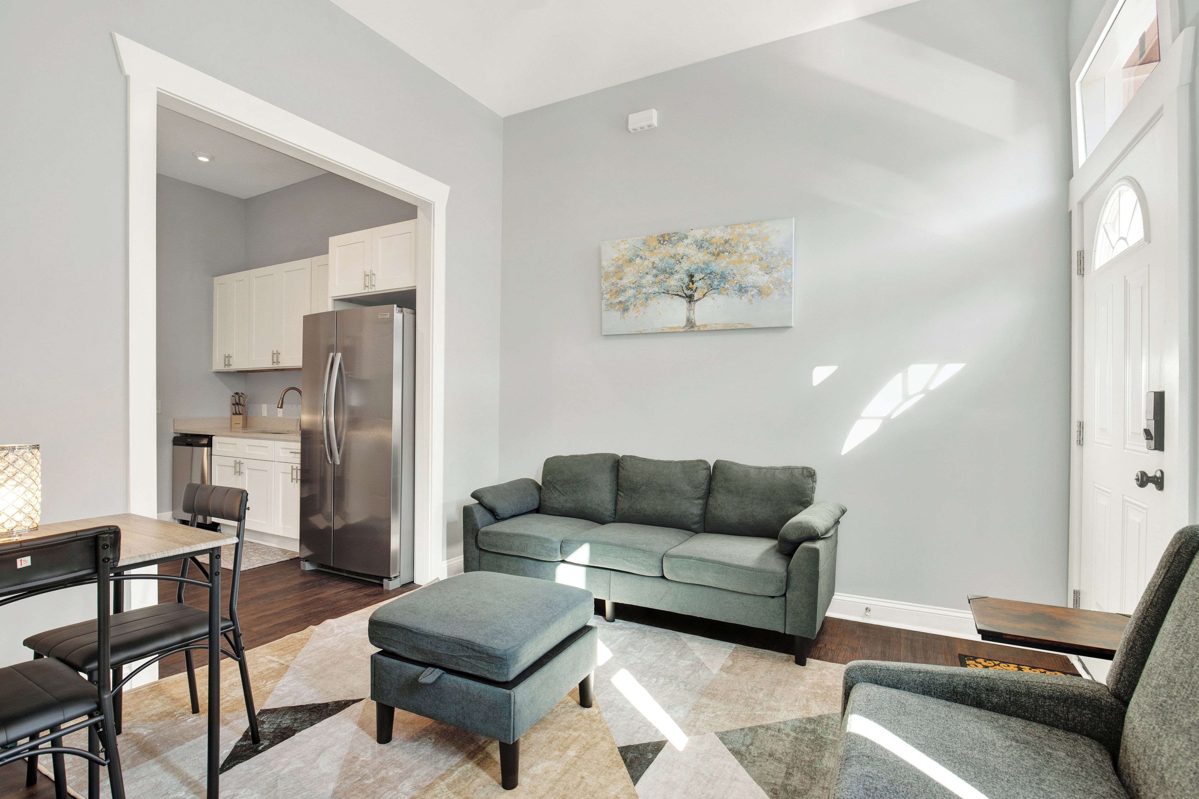 A modern living room with a grey sofa, a dining table with chairs, and a kitchen in the background.
