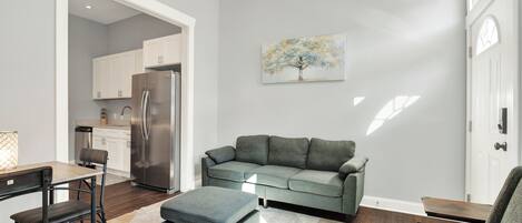 A modern living room with a grey sofa, a dining table with chairs, and a kitchen in the background.