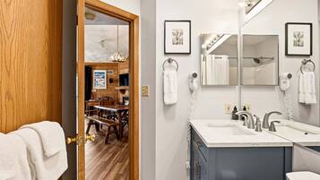 A bathroom with dual sinks, a large mirror, and a wooden door leading to a dining area.