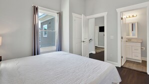 Ein Schlafzimmer mit einem großen Bett, ein Badezimmer mit Waschtisch und Spiegel sowie eine Tür zu einem weiteren Raum.
