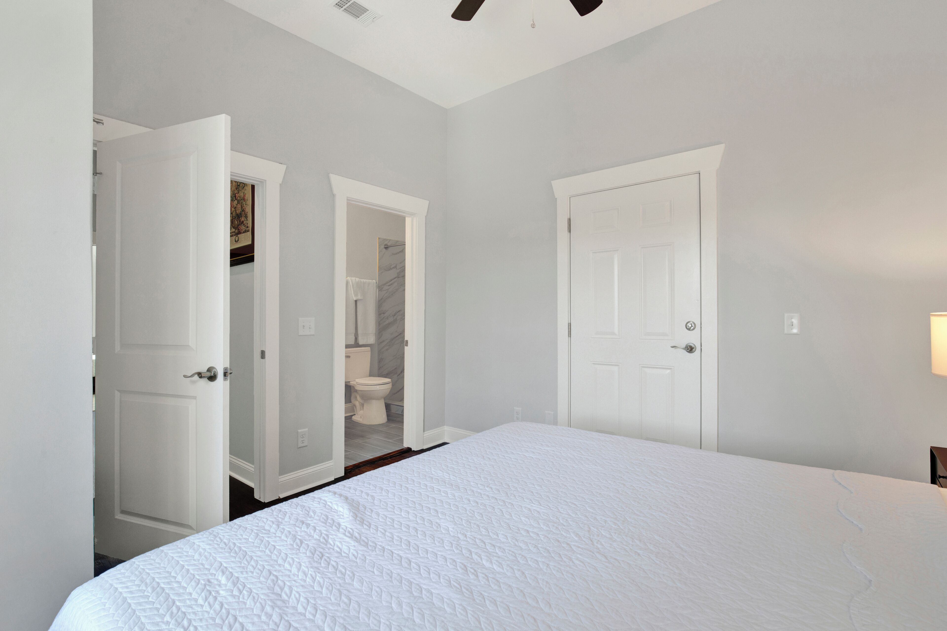 A bedroom with a large bed, two doors leading to a bathroom, and a ceiling fan.