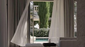 A modern room with a large window, white curtains, a small table, and a seating area. - Lantana Villas and Hotel (Pegeia)