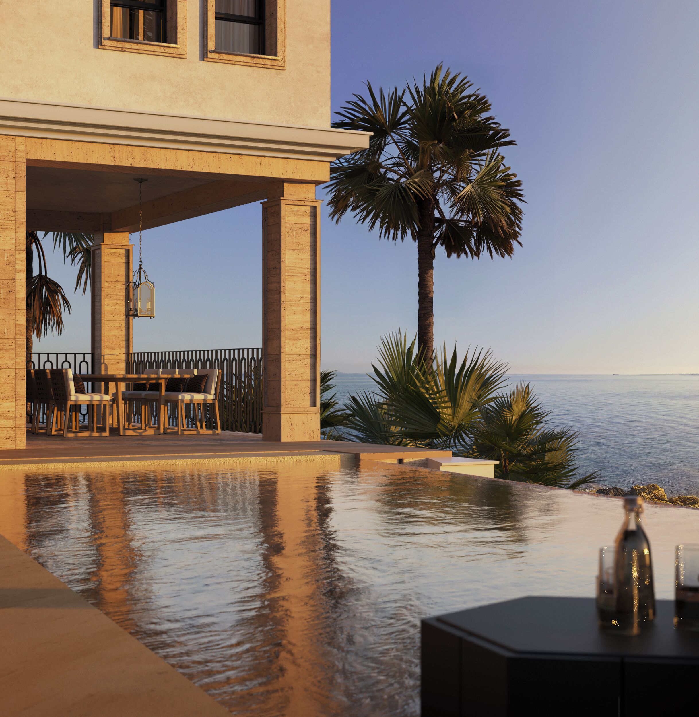 A poolside area with a table and chairs, a palm tree, and a view of the sea.