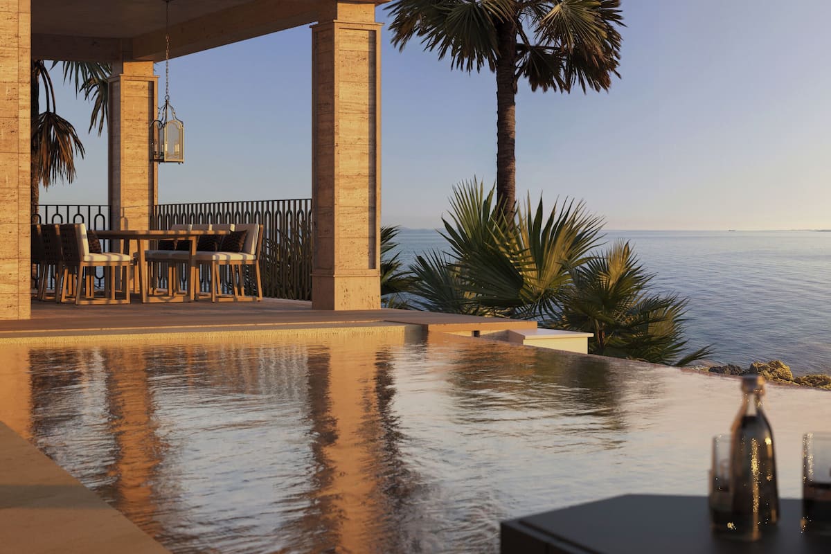 Un espace aménagé au bord de la piscine, avec une table et des chaises, un palmier et une vue sur la mer.