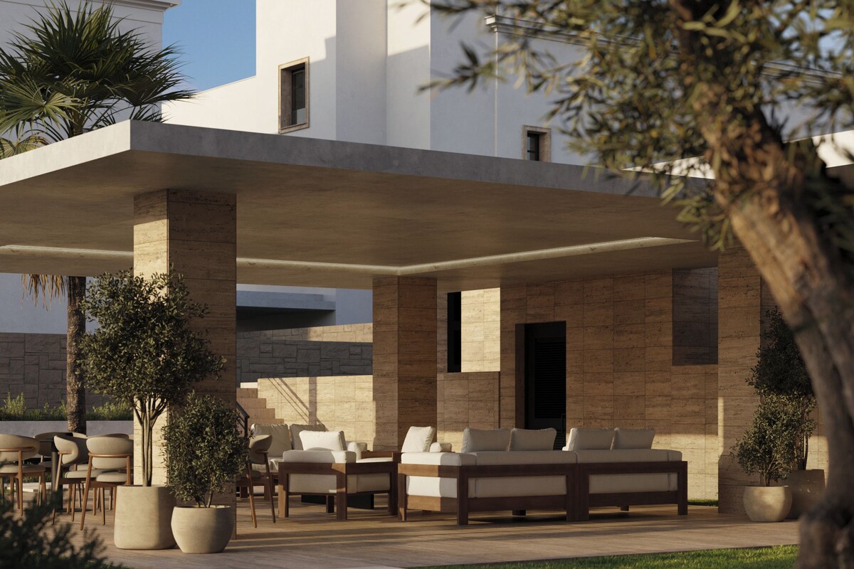 A modern outdoor seating area with a stone wall, a wooden deck, and a large tree in the foreground.