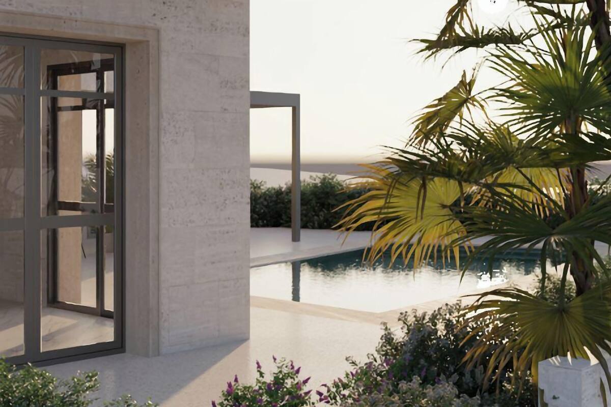 Un bâtiment moderne doté d’une porte en verre, d’une piscine et de plantes tropicales.