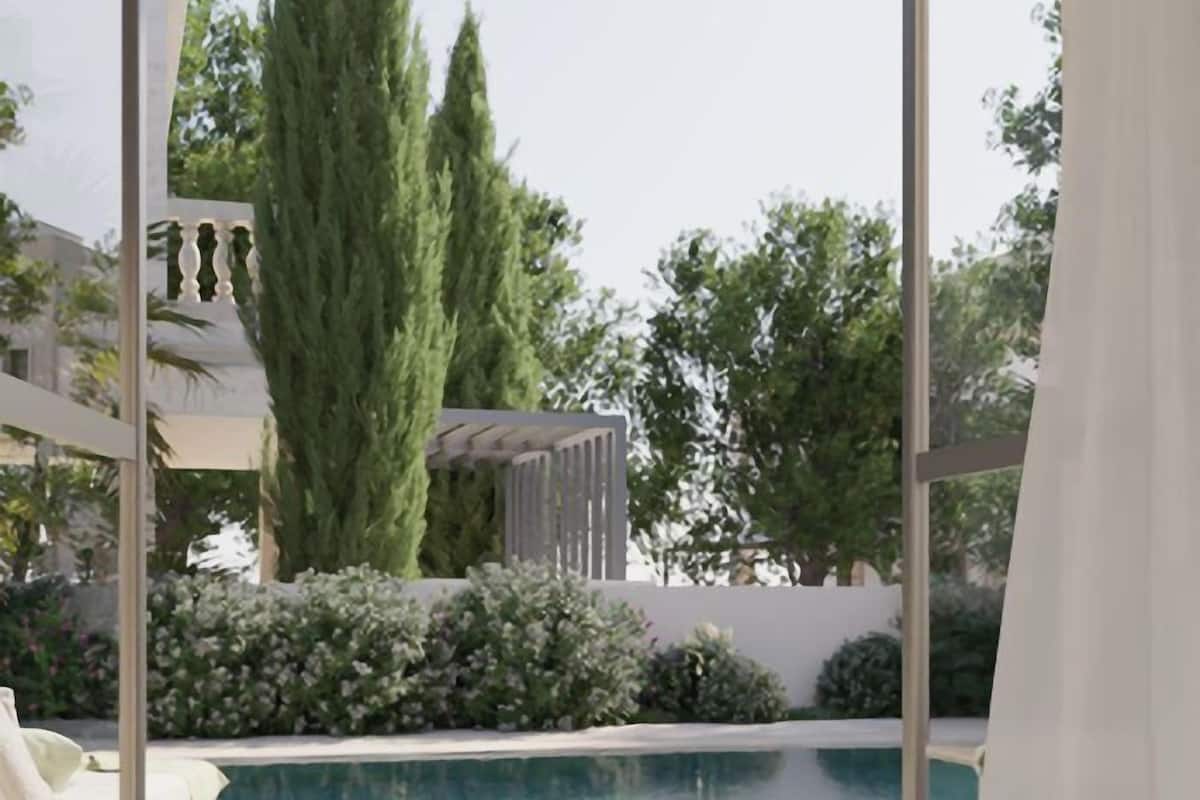 Un espace piscine extérieur moderne, offrant une vue dégagée sur le ciel, entouré de verdure et bordé d’un bâtiment blanc.