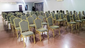 A conference room with rows of chairs and tables, a podium, and an air conditioning unit on the wall. - Acamms Lodge (Lusaka)