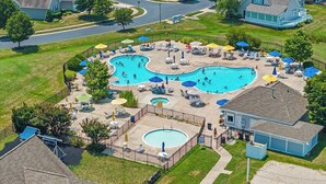 Ein Wohngebiet-Schwimmbecken mit mehreren Bereichen, umgeben von Liegestühlen und Sonnenschirmen, neben einem Haus.