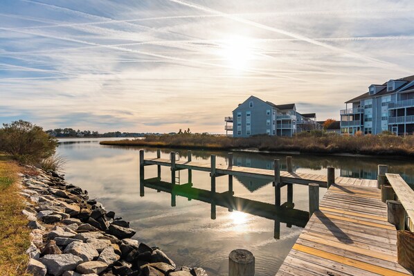 A waterfront property with a wooden dock, a building with multiple balconies, and a calm lake. - Bay Breeze Retreat/Beautiful 2 bedroom sleeps 7 (Ocean View)