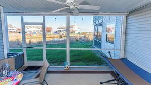 Eine überdachte Terrasse mit Deckenventilator, großen Fenstern, einem Tisch mit Stühlen und einer Hängematte.