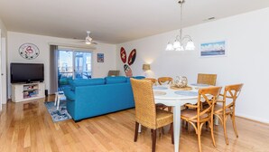 Ein Wohnzimmer mit blauem Sofa, einem Esstisch mit Stühlen, einem Fernseher und einem Deckenventilator.