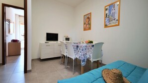 Ein Zimmer mit einem Bett, einem Schreibtisch mit Computer, einem Stuhl, einem Tisch mit Tischdecke und zwei gerahmten Bildern an der Wand.