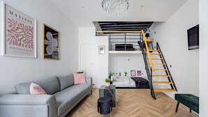 En moderne stue med en grå sofa, et sort sofabord, parketgulv i fiskebensmønster, en trappe i sort træ og en lysekrone.