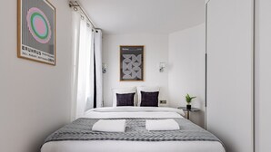Et moderne hotelværelse med en pænt redt seng, et lille natbord med en lampe og en potteplante.