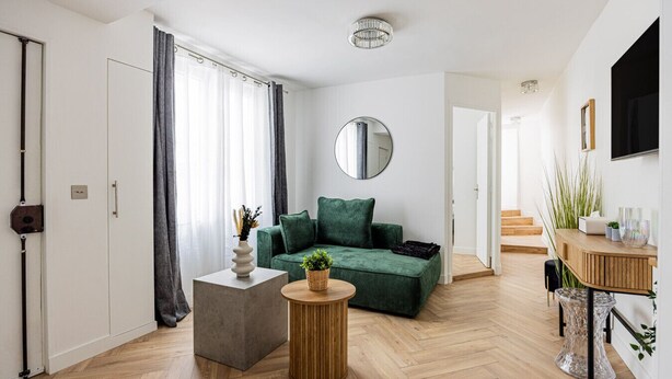 En moderne stue med en grøn sofa, et rundt spejl og et træbord.