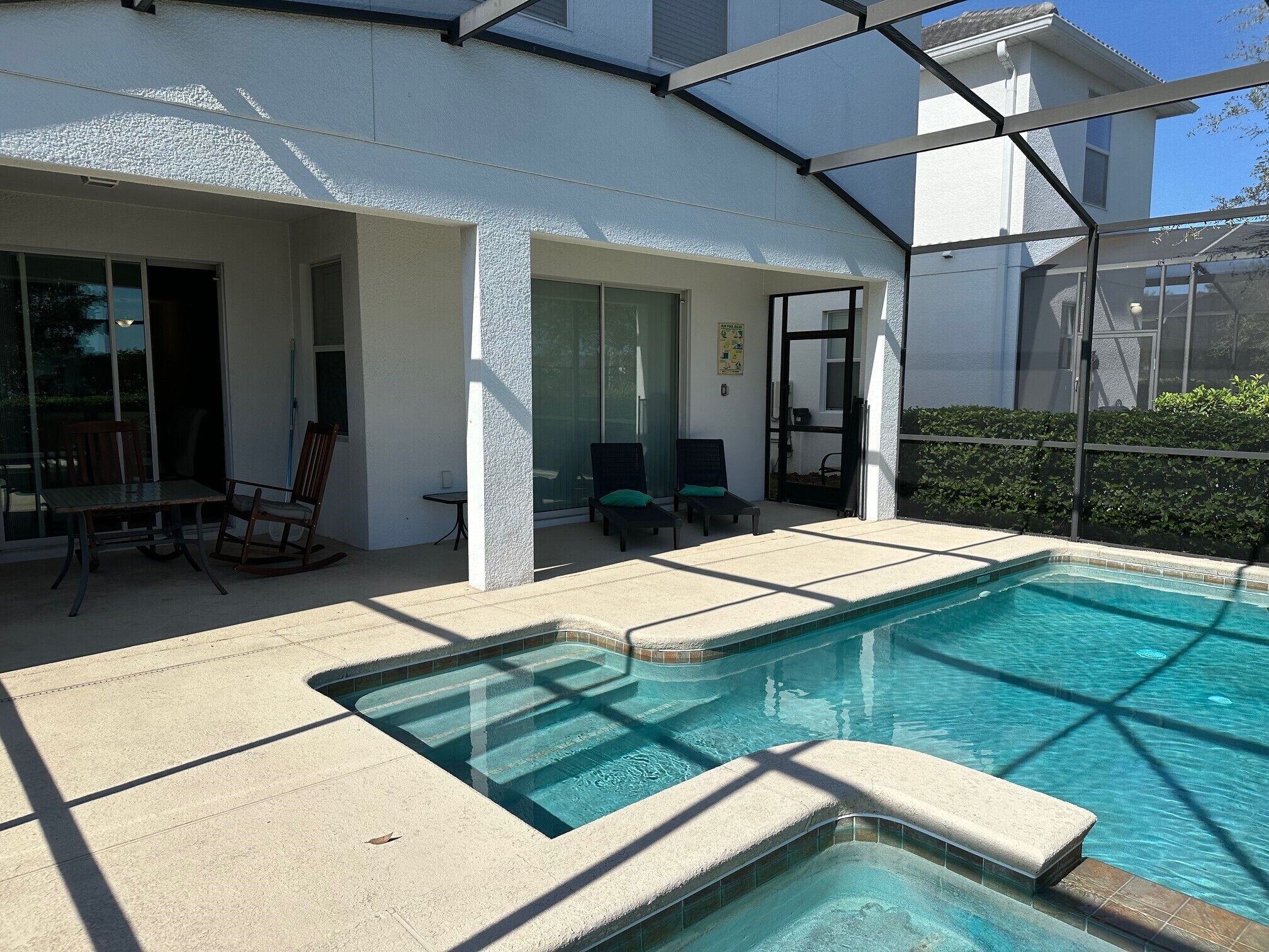 Ein Pool mit einer abgesenkten Liegeinsel, umgeben von einer überdachten Terrasse mit Stühlen und Tisch.