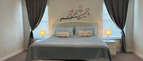 Un dormitorio con una cama, dos lámparas de noche, una ventana con persianas y un adorno en la pared.
