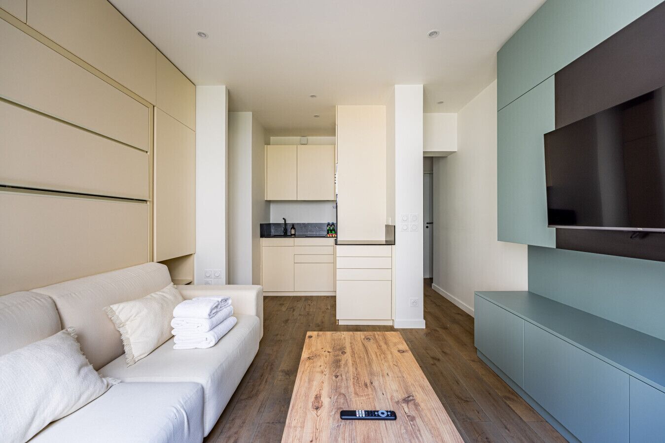 Una habitación de hotel moderna con sofá, una mesa de centro de madera y televisor montado en la pared.