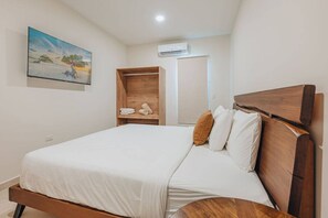 A bedroom with a wooden bed frame, white bedding, a wooden wardrobe, and a painting on the wall. - Super Stylish Home with Private Pool and outdoor (Noord)