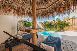 Un espace aménagé au bord de la piscine, doté d’un toit de chaume, de chaises longues et d’une petite piscine.
