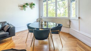 Ruokailutilassa on pyöreä pöytä ja neljä tuolia, sohva sekä ikkuna, josta avautuu näkymä puihin.