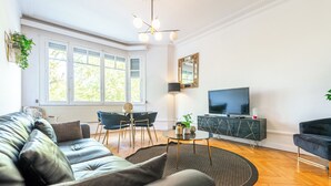 Moderni olohuone, jossa on nahkasohva, ruokapöytä tuoleineen, televisio ja suuri ikkuna, josta tulee runsaasti luonnonvaloa.