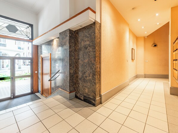 En modern hotellobby med en marmordisk i receptionen, en entré med glasdörr och ett klinkergolv.