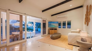 A modern living room with a large sliding glass door leading to an outdoor dining area, a flat-screen TV, and a cozy seating arrangement. - NEW: Oceanfront Villa w/Private HotTub and Pool (Noord)