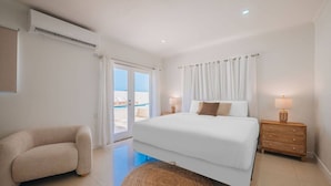 A bedroom with a bed, a chair, a nightstand, and a view of the outside. - NEW: Oceanfront Villa w/Private HotTub and Pool (Noord)