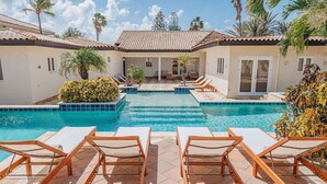 A pool area with lounge chairs, a tiled deck, and a building with a tiled roof. - NEW: Oceanfront Villa w/Private HotTub and Pool (Noord)