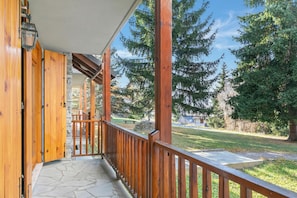 Un portico in legno con pavimento in pietra, una ringhiera e vista su una zona erbosa con alberi.