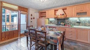 A kitchen with wooden cabinets, a dining table set for four, and a view through the open door to the outside. - Appartamento I 2 Pini for 6 With Balcony (Sauze d'Oulx)