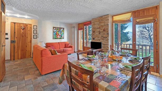 A dining area with a table set for four, a sofa, and a TV in the background. - Appartamento I 2 Pini for 6 With Balcony (Sauze d'Oulx)