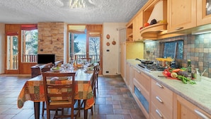 A kitchen with wooden cabinets, a stone wall, and a dining area with a table set for four. - Appartamento I 2 Pini for 6 With Balcony (Sauze d'Oulx)